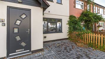 En bostadsbyggnad med en mörkfärgad ytterdörr, ett litet fönster och en gång av tegelstenar som leder fram till entrén.