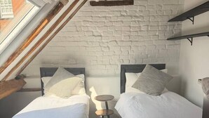 Et værelse med to senge, et lille rundt bord og et skråt loft med synlige bjælker.