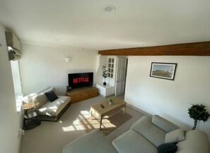 A living room with a sofa, a coffee table, a TV displaying 'NETFLIX', and a door leading to another room. - Cosy & spacious 3BR by Warwick castle (Warwickshire)