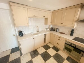 A compact kitchen with a checkered floor, a sink, a stove, and cabinets. - Cosy & spacious 3BR by Warwick castle (Warwickshire)