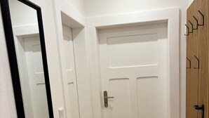 Um corredor com porta branca, espelho e parede revestida de madeira.