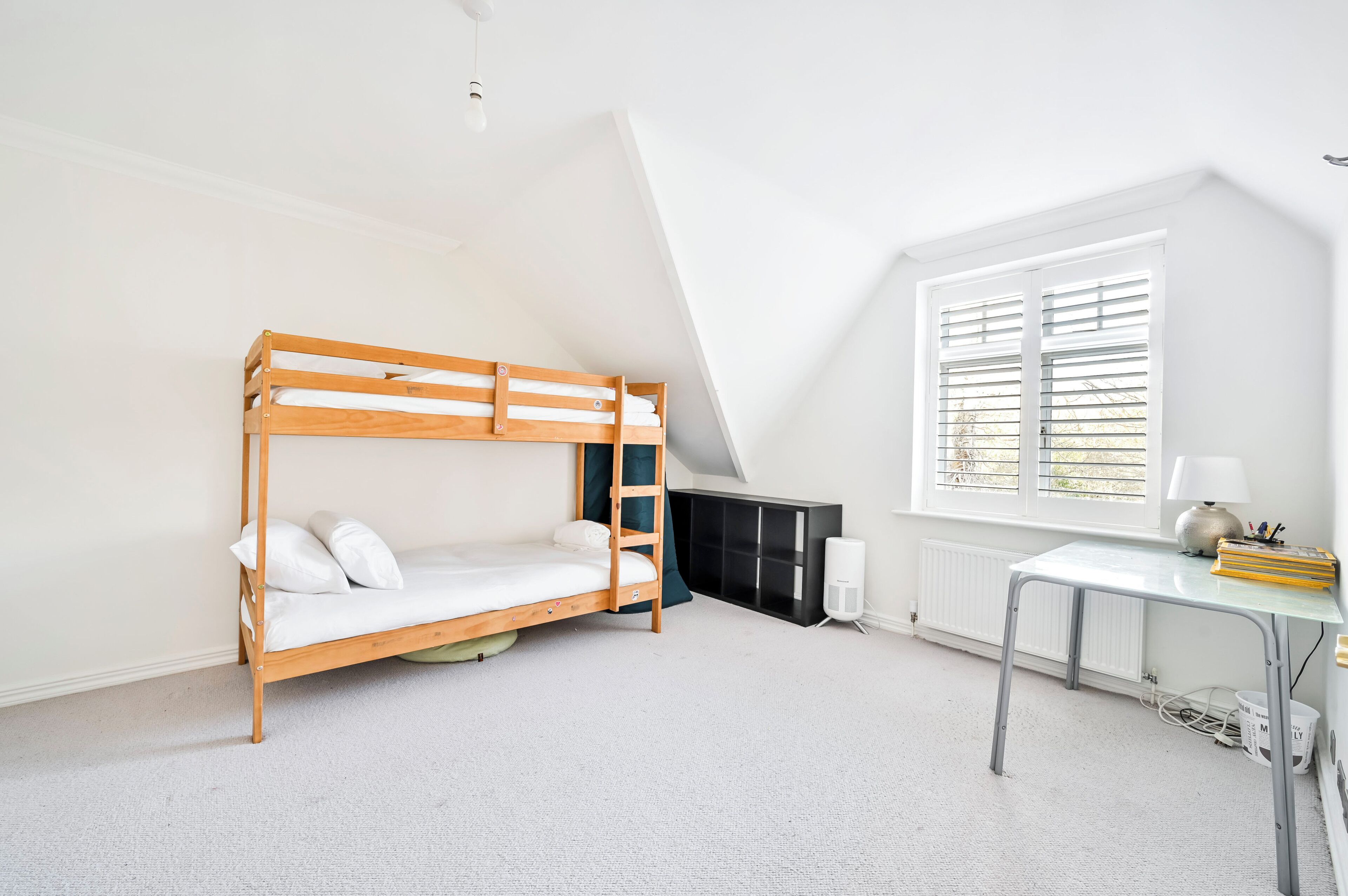 A room with a bunk bed, a desk, a radiator, and a window with blinds.
