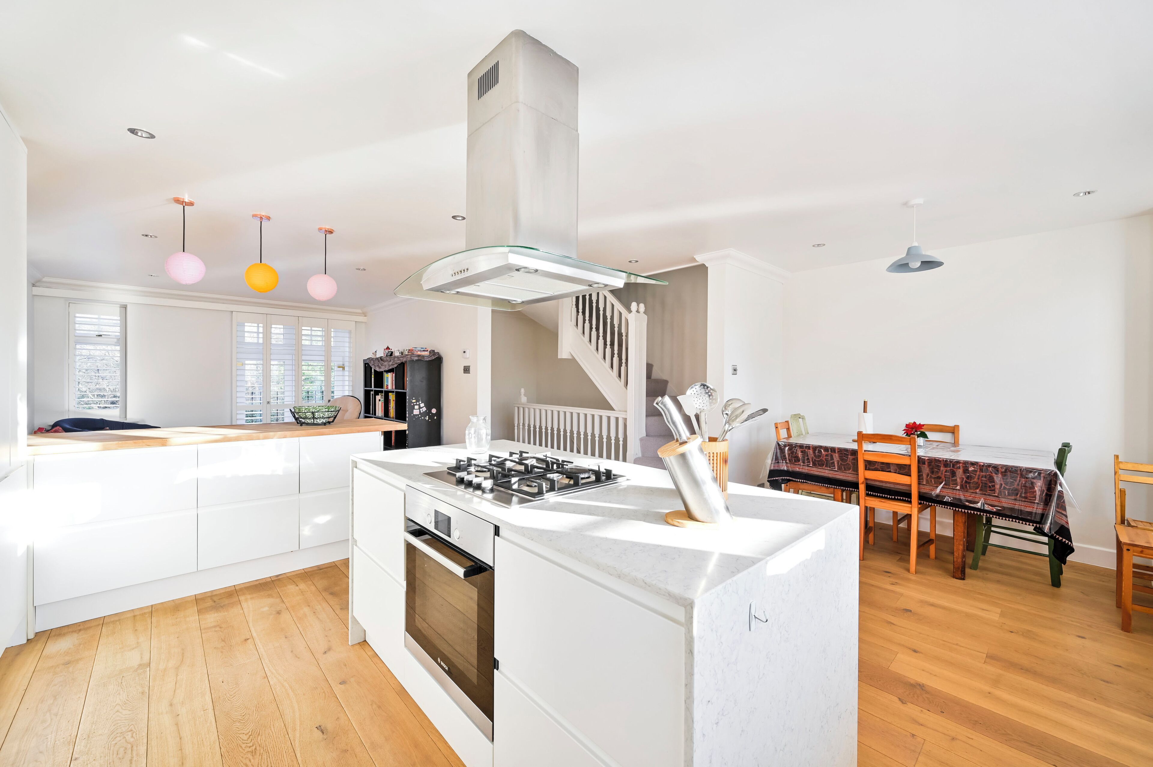 A modern kitchen with a central island, built-in oven, and a dining area with a table and chairs.