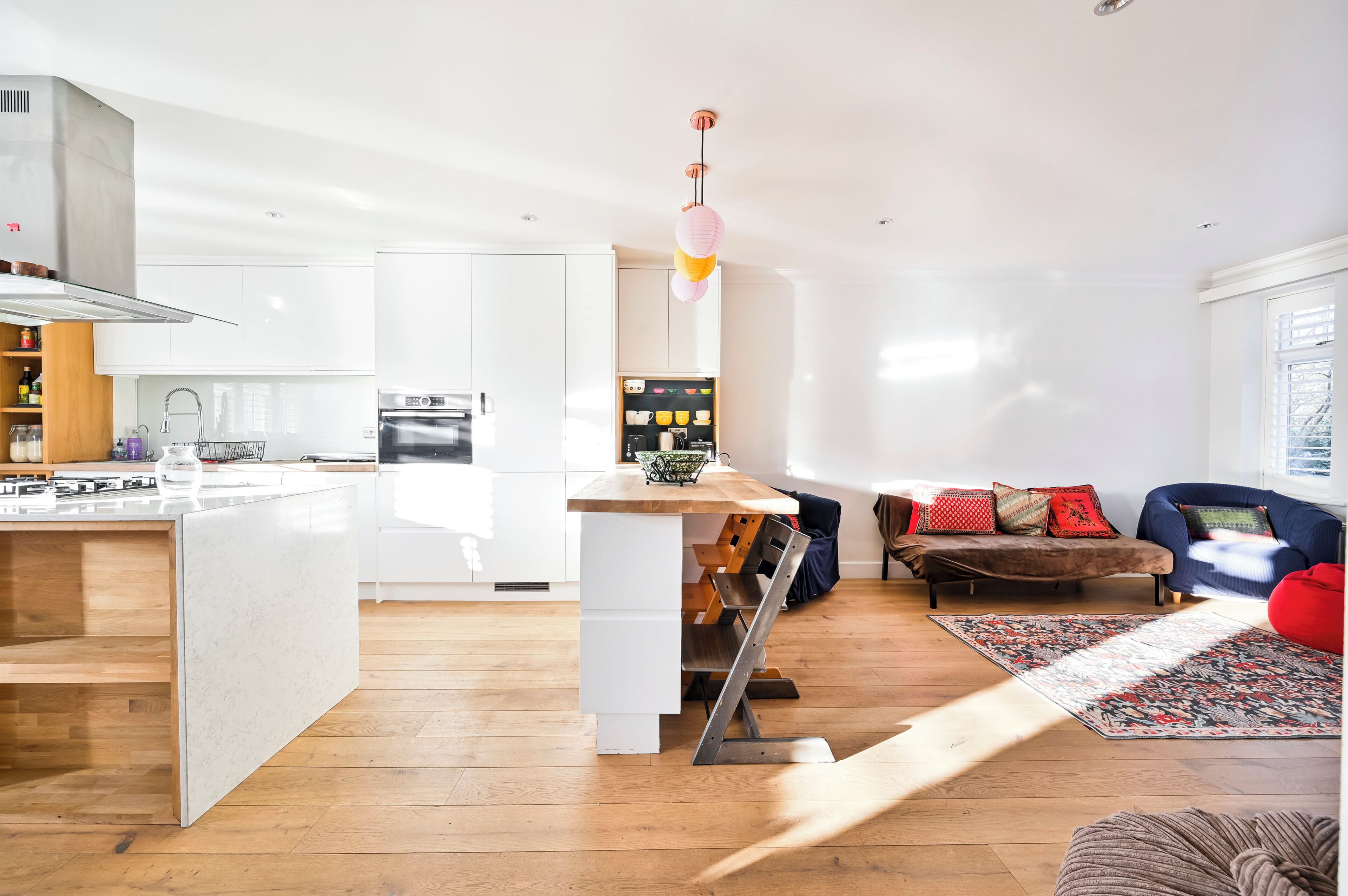 A modern kitchen with white cabinetry, a central island, and a dining area with a blue sofa and patterned rug.