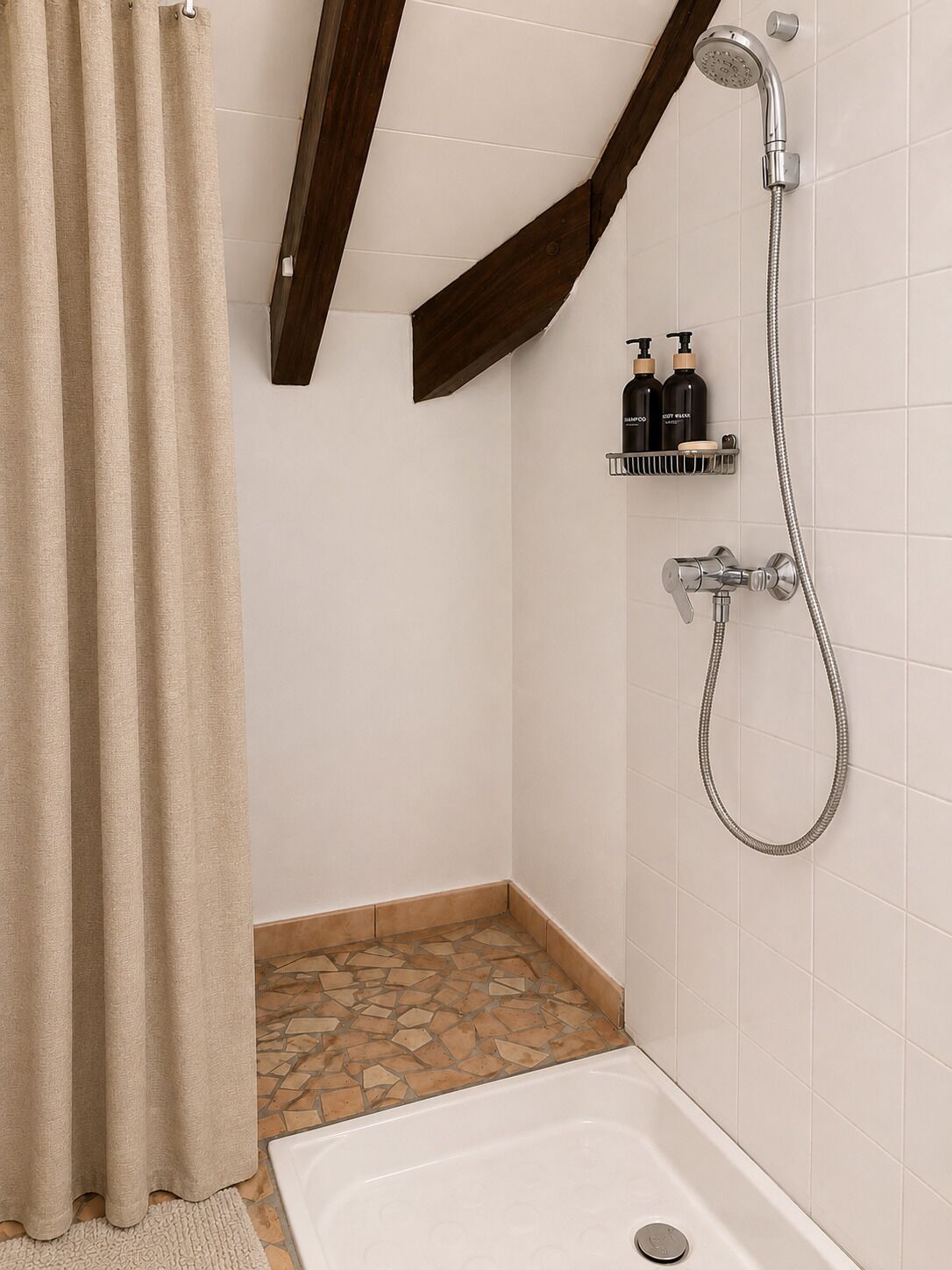 Ein Duschbereich mit Duschkopf, Handbrause und am Wand montiertem Wasserhahn. Eine Ablage mit Pflegeprodukten und ein teilweise geöffneter Duschvorhang.