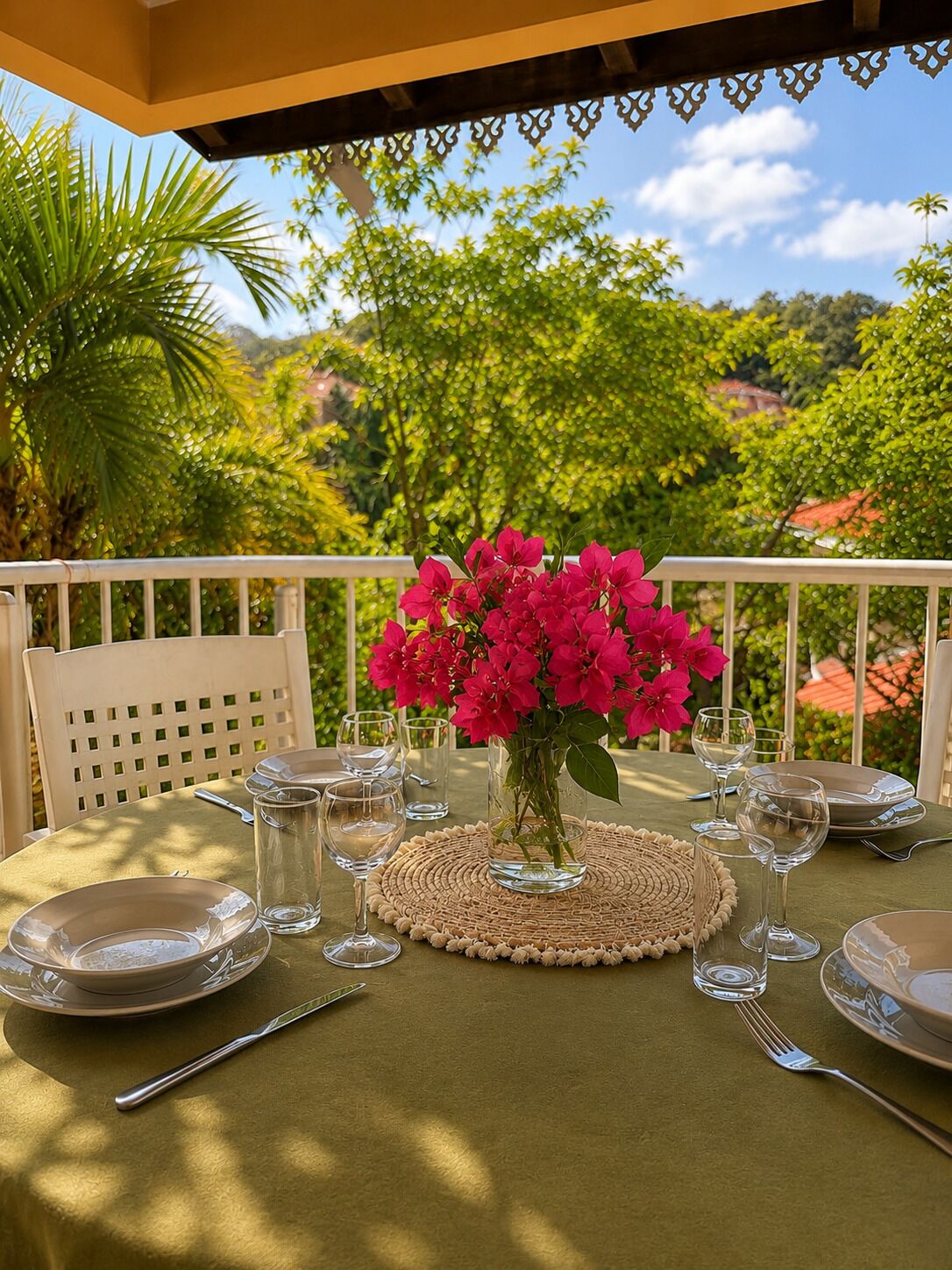 Un espacio exterior para comer con una mesa dispuesta para dos personas, rodeado de abundante vegetación y un cielo despejado.