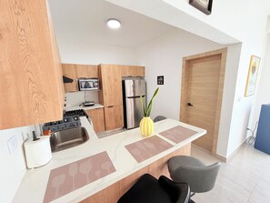 A modern kitchen with wooden cabinets, stainless steel appliances, a marble countertop, and a small seating area with chairs. - Private Pool Villa. 3BR Near Bávaro Beach. Sleeps 8 (Punta Cana)