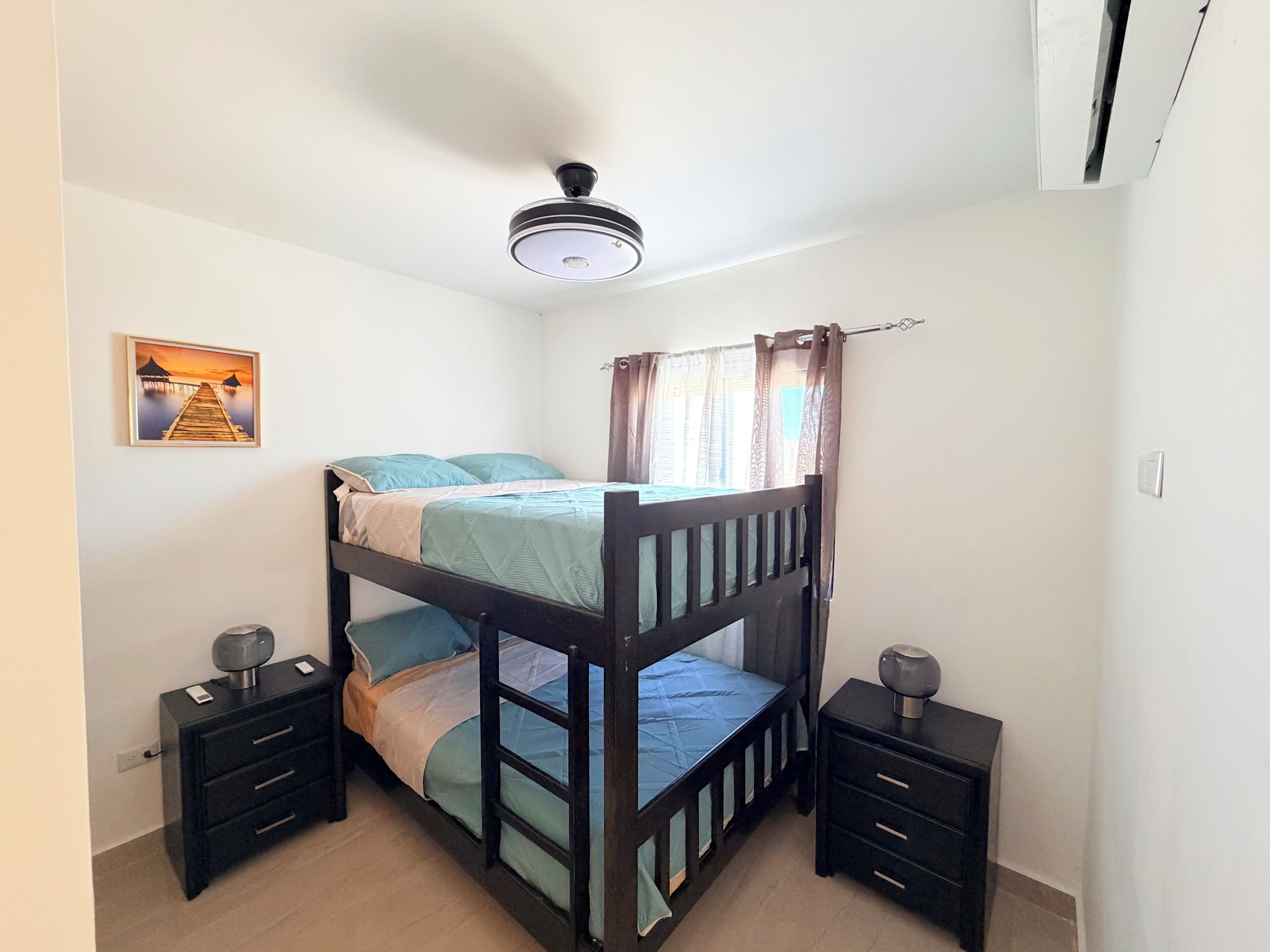 A bunk bed room with a ceiling fan, bedside tables, and a painting on the wall.