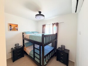 Une chambre avec un lit superposé, un ventilateur de plafond, des tables de chevet et un tableau au mur.