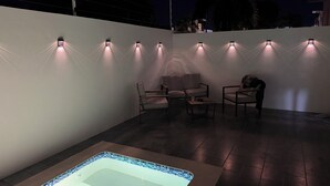 Ett poolområde med ett bubbelbad, sittplatser och väggmonterad belysning.