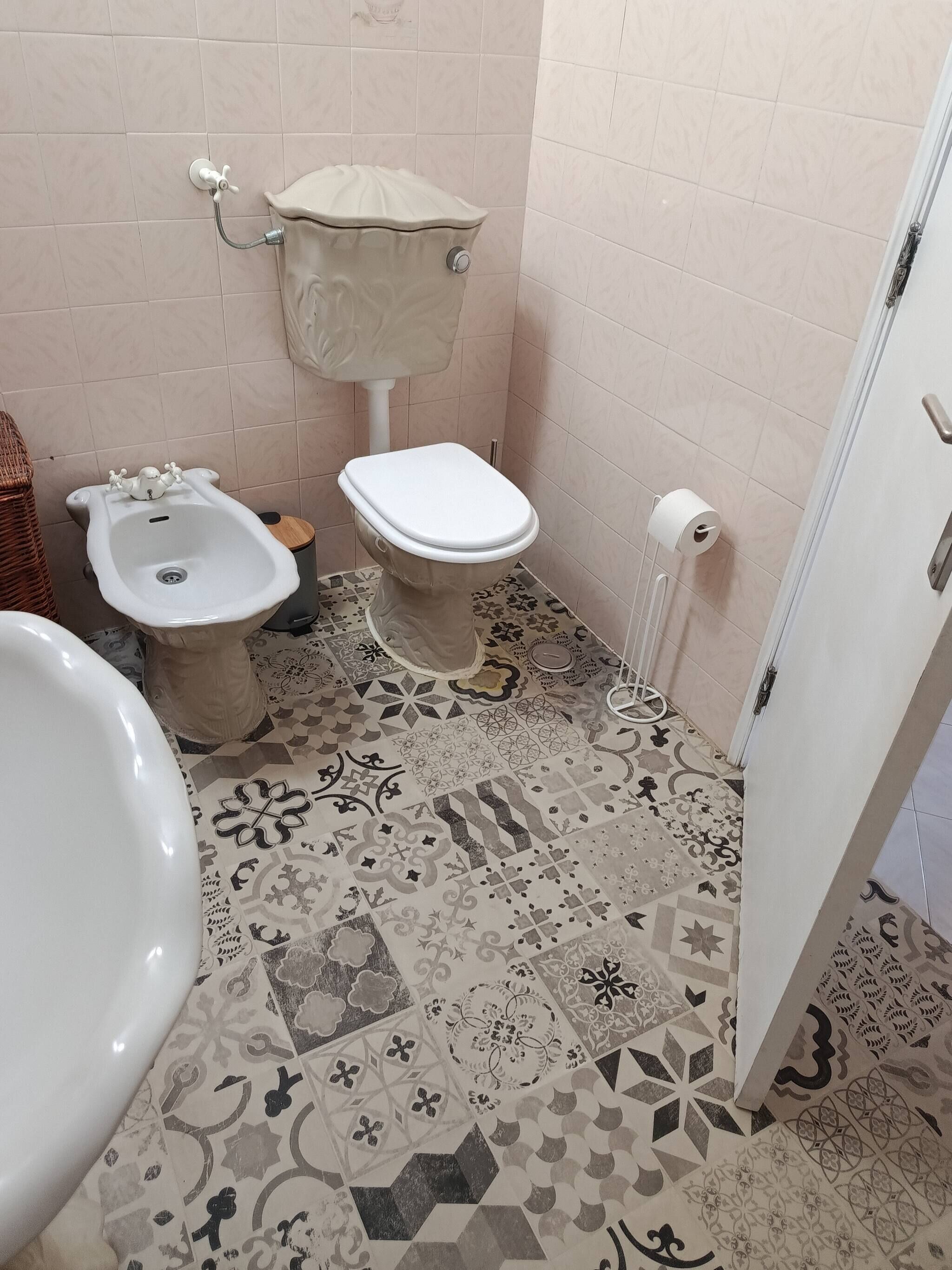 Une salle de bain comprenant des toilettes, un bidet et un lavabo. Le sol est recouvert de carreaux à motifs.