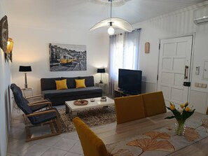 Ein Wohnzimmer mit einer Couch, Sesseln, einem Couchtisch, einem Fernseher und einem Gemälde an der Wand.