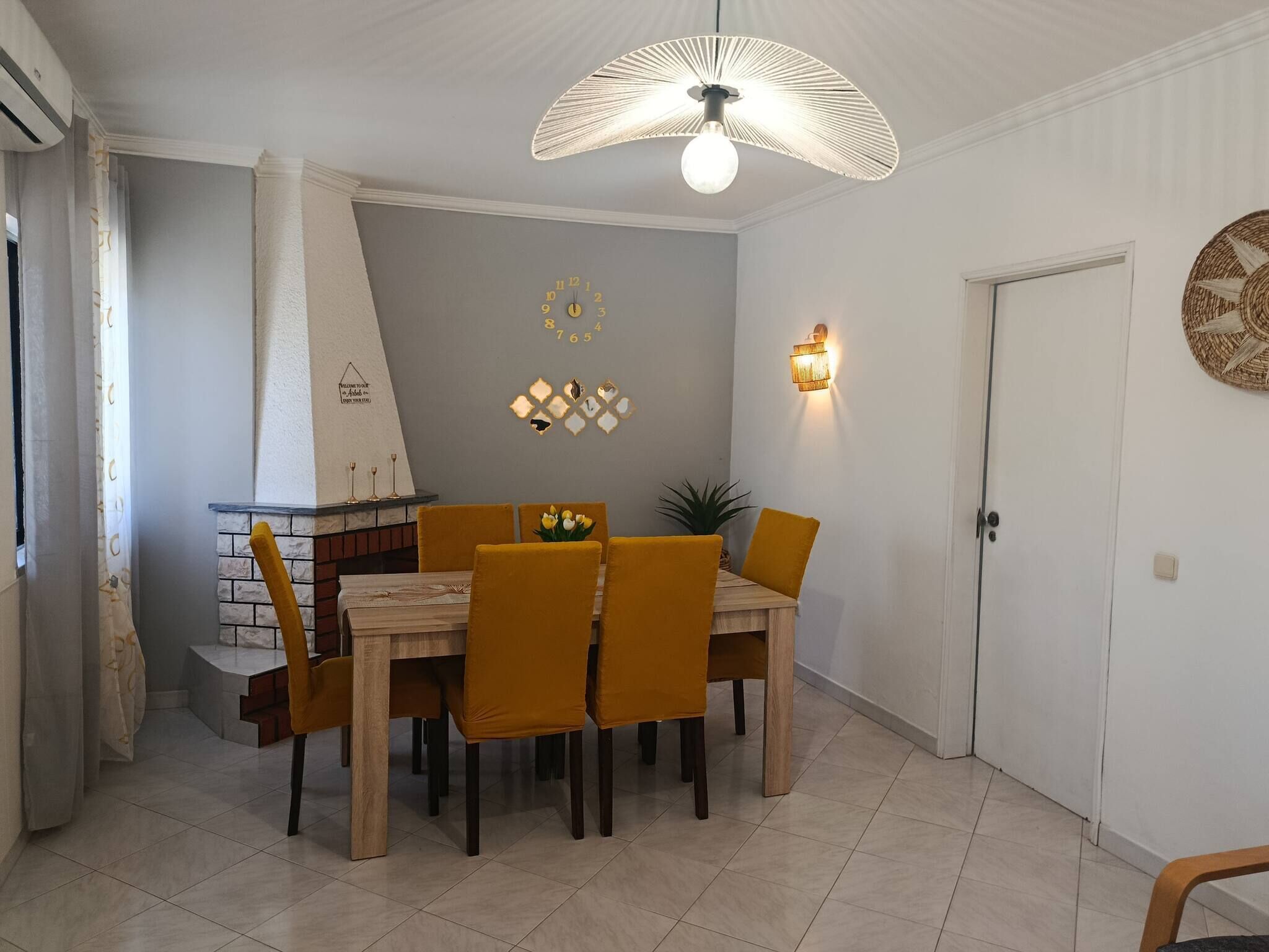 A dining area with a table and chairs, a decorative wall clock, and a unique ceiling light fixture.