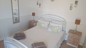 A neatly made bed with pillows and folded towels, a bedside table with a lamp, a nightstand, and a wall-mounted mirror. - T2 Magnificent Views (Faro)