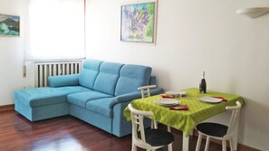 Une pièce avec un canapé bleu, une table à manger recouverte d’une nappe verte et des chaises blanches.