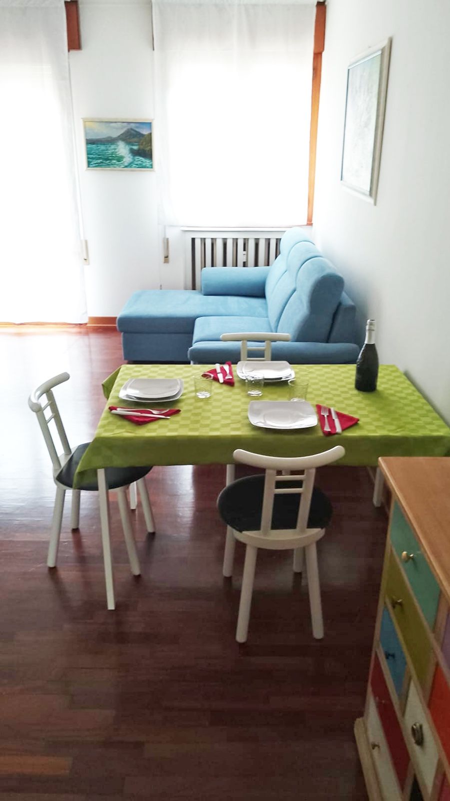 A dining area with a table set for two, a blue sofa in the background, and a radiator on the wall.