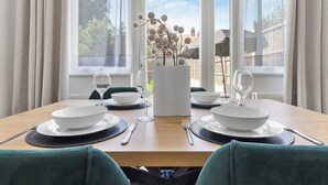 A dining table set for four with white plates, cutlery, and a vase with branches. - Perfect Location near Heathrow & 2 min London Tube (Hounslow)