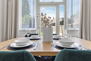 A dining table set for four with white plates, cutlery, and a vase with branches. - Perfect Location near Heathrow & 2 min London Tube (Hounslow)