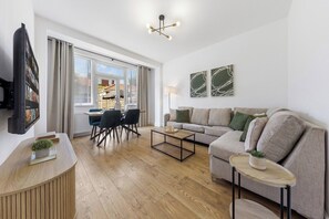 A modern living room with a sofa, coffee table, and TV. - Perfect Location near Heathrow & 2 min London Tube (Hounslow)