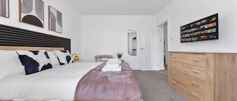 A bedroom with a bed, a wooden dresser, a wall-mounted TV, and a ceiling light fixture.