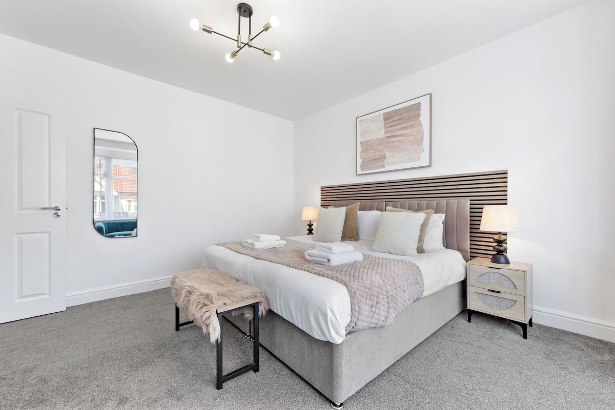A bedroom with a bed, bedside tables, a mirror, a ceiling light fixture, and a framed artwork on the wall.