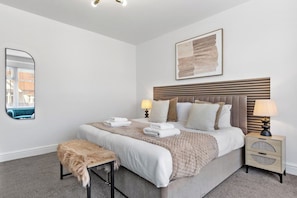 A bedroom with a bed, bedside tables, a mirror, and a wall art piece. - Perfect Location near Heathrow & 2 min London Tube (Hounslow)