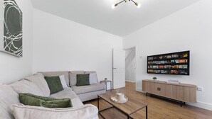 A modern living room with a sofa, coffee table, TV, and a wooden cabinet. - Perfect Location near Heathrow & 2 min London Tube (Hounslow)