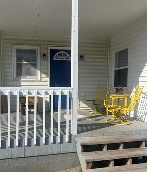 A porch with a white railing, a blue door, and yellow chairs.