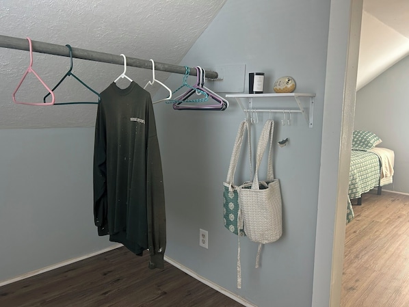 A room with a clothing rack, a shelf with a bottle and a decorative item, and a bed with a patterned blanket.