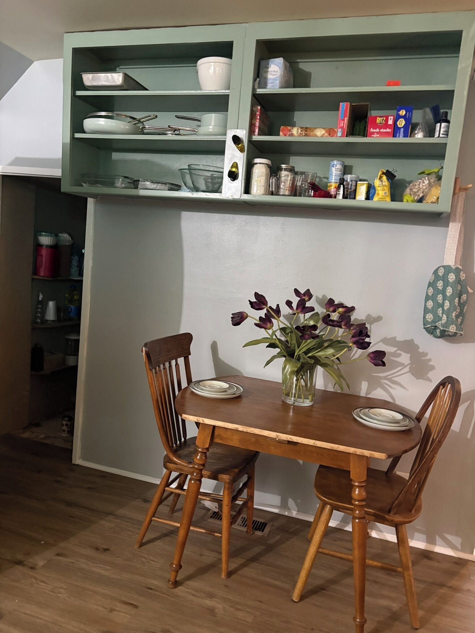 Una mesa de comedor con sillas, un florero con flores y una estantería en la cocina con varios objetos.