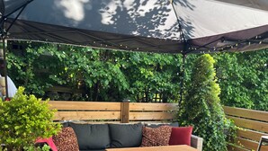 Eine Terrasse im Freien mit Holztisch, gepolsterten Sitzgelegenheiten und einem großen Sonnenschirm.