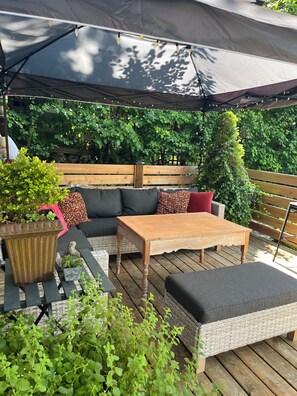 An outdoor patio with a wooden table, cushioned seating, and a large umbrella. - Charming little cottage minutes from town (Gibsons)
