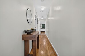 A hallway with a wooden console table, a mirror, and a door leading to a room. - Cozy Traveler's Dream Near NYC & PATH w/ Private Parking (Jersey City)