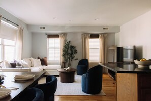 A modern living room with a sofa, chairs, a coffee table, and a TV. - Cozy Traveler's Dream Near NYC & PATH w/ Private Parking (Jersey City)