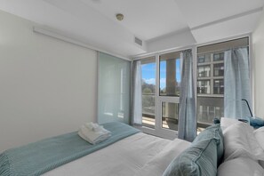 Habitación de hotel con cama, ventana con cortinas, vista a la ciudad y puerta que da a un espacio exterior.