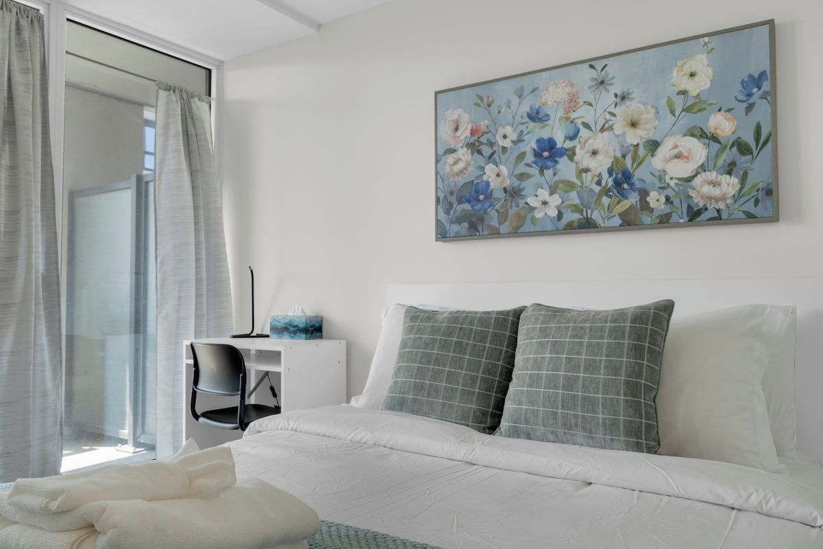 A hotel room with a bed, a desk, and a painting of flowers on the wall.