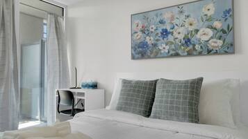 A hotel room with a bed, a desk, and a painting of flowers on the wall.