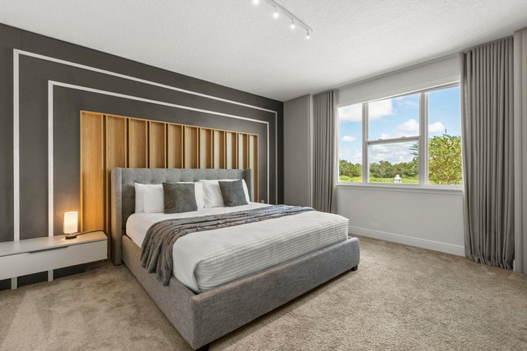 Une chambre à coucher moderne avec un grand lit, une table de chevet, une lampe de chevet et une vue sur l’extérieur par une fenêtre.