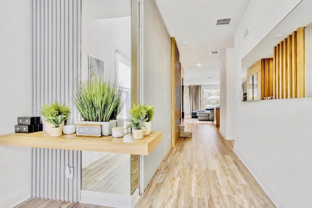 Un interior moderno con suelo de madera, una estantería empotrada con plantas y una cocina al fondo.
