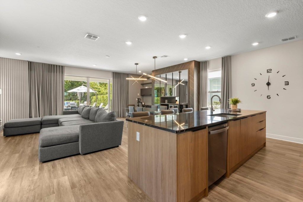 A modern kitchen with a central island, a dining area with a sofa, and a large window with curtains.