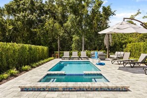 A rectangular swimming pool with a tiled edge, surrounded by a paved deck. There are lounge chairs and a covered umbrella area. - Bear's Den at Reunion - Luxury 4BD/3BA (836 DM) (Kissimmee)