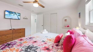 Un dormitorio con cama, ventilador de techo, televisor, cómoda y ventana.