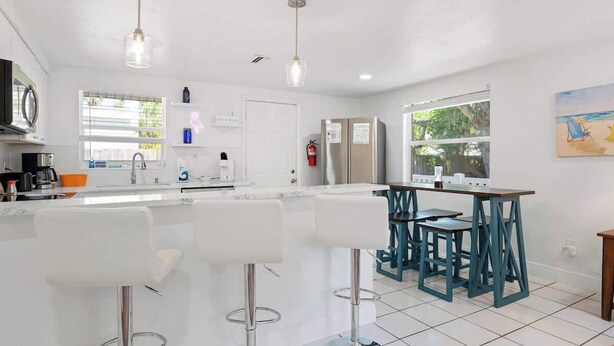 Una cocina moderna con encimeras blancas, electrodomésticos de acero inoxidable y taburetes de bar.