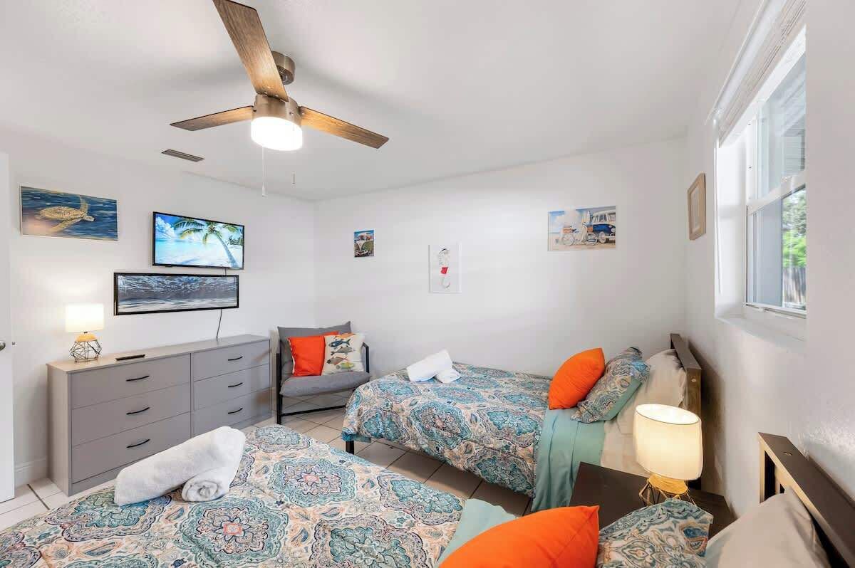 Une chambre avec deux lits, un ventilateur de plafond, une commode et des œuvres d’art accrochées aux murs.