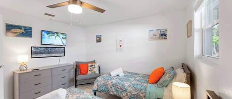 Une chambre avec deux lits, un ventilateur de plafond, une commode et des œuvres d’art accrochées aux murs.