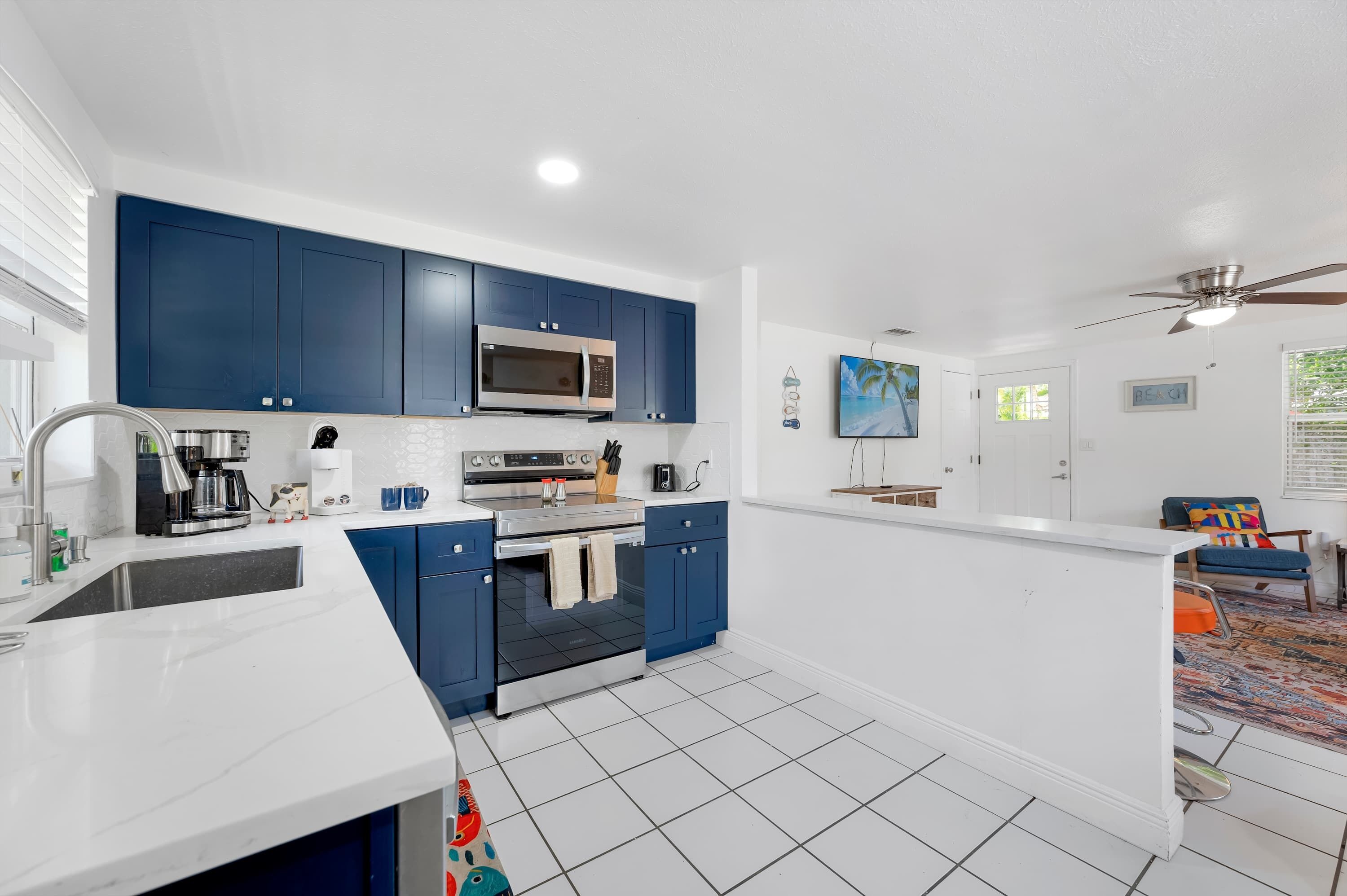 A modern kitchen with blue cabinets, a microwave, a coffee maker, and a large island with a sink.