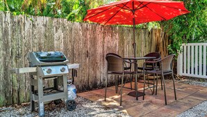 Eine Terrassengruppe im Freien mit Grill, Stühlen und einem roten Sonnenschirm.