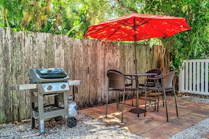 Eine Terrassengruppe im Freien mit Grill, Stühlen und einem roten Sonnenschirm.