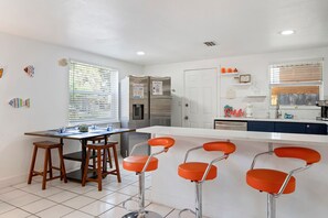 A modern kitchen with a central island, bar stools, and a dining table. - Aeon Suite Bike/Walk Dtwn 2BR, Grill, Patio & Pups (Sarasota)