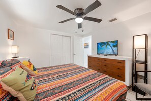 Een slaapkamer met een bed, plafondventilator, dressoir, televisie en bedlamp.